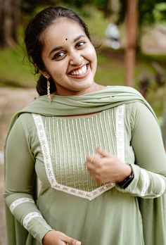 a woman in a green dress smiling and holding something up to her chest with both hands