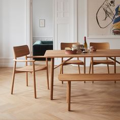 a wooden table with two chairs and a bench in front of it, next to a painting on the wall