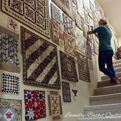 a woman standing on the stairs in front of a wall full of quilts