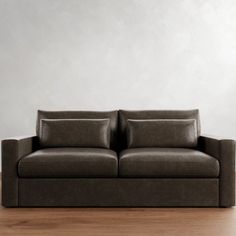 a brown couch sitting on top of a hard wood floor next to a white wall