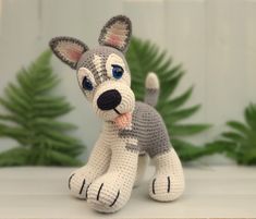 a crocheted gray and white dog sitting on top of a table next to plants