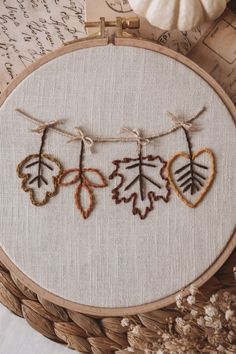 an embroidery project with leaves and hearts hanging on a string in front of a basket