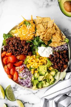 a bowl filled with taco salad and tortilla chips next to an avocado