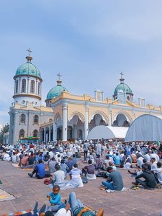 many people are sitting on the ground in front of a large building with blue domes