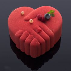 a cake shaped like a heart with berries and leaves on it's side sitting on a black surface