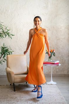 a woman in an orange dress standing next to a chair