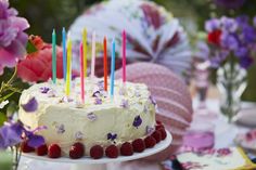 a birthday cake with white frosting and colorful candles on it, surrounded by flowers