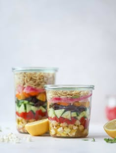 two mason jars filled with pasta salad and lemon wedges next to each other on a white surface