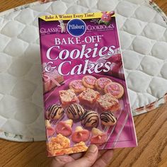 a box of cookies and cakes sitting on top of a wooden table next to a person's hand