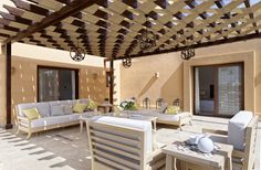 an outdoor living area with white couches and chairs under a pergolated roof