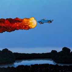 a blue car flying through the air next to an orange fireball on top of a lake