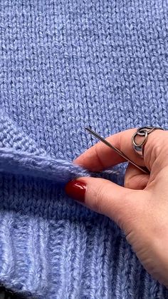 a woman's hand holding a pair of scissors over a blue knitted blanket