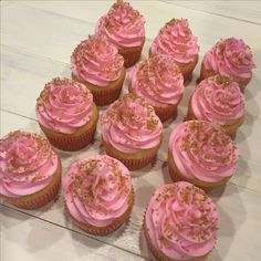 cupcakes with pink frosting and sprinkles arranged on a table