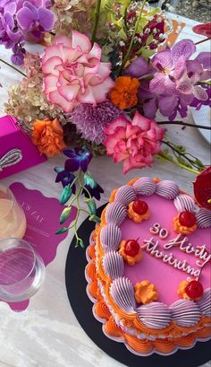 a pink birthday cake sitting on top of a table next to some flowers and candles