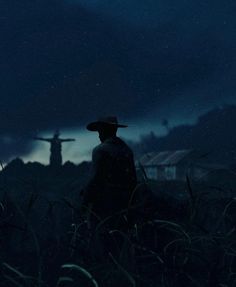 a man with a hat standing in the middle of a cornfield at night under a cloudy sky