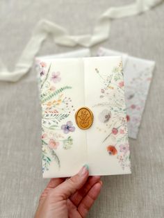 a hand holding an open book with a gold button on it and flowers all over the pages