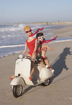 two dolls are sitting on top of a scooter at the edge of the beach