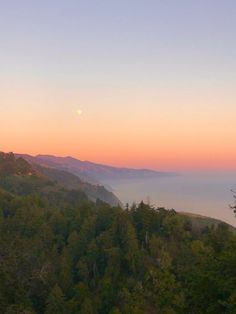 the sun is setting over some trees and mountains in the distance, as seen from an overlook