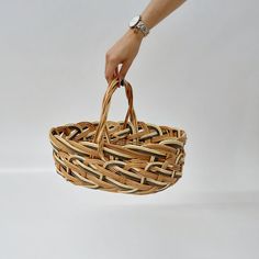 a woman's hand is holding a woven basket with two handles, on a white background