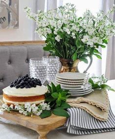 a table topped with a cake covered in frosting and lots of greenery next to a vase filled with white flowers