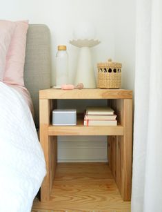 a small wooden table with books on it next to a white bed and pink pillows