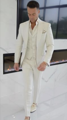 a man in a white suit is standing near a fireplace and looking down at his shoes