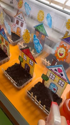 children's hands holding up small houses made out of dirt and soil in front of a window