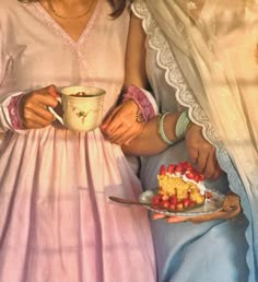 two women in pink dresses are eating cake and drinking coffee