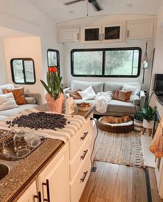 a kitchen and living room area in a mobile home with wood floors, white walls, and windows