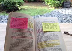 an open book with sticky notes attached to it sitting on a table in front of a garden