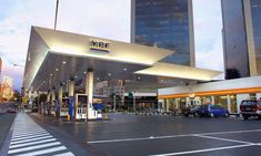 an empty gas station with cars parked at it's entrance and tall buildings in the background