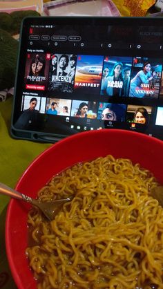 a red bowl filled with noodles next to a laptop