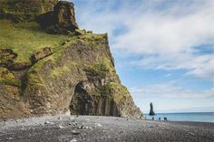 people are walking on the beach near some cliffs