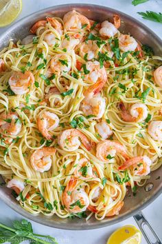 pasta with shrimp and parsley in a pan next to lemon wedges on the side