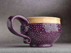 a purple and yellow ceramic cup sitting on top of a gray tableclothed surface