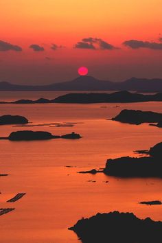 the sun is setting over an ocean with small islands in the water and mountains in the distance