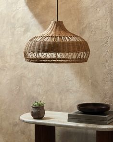 a wicker lamp hanging from the ceiling next to a table with a bowl on it