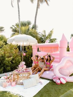 two women sitting on an inflatable pool with pink decorations and umbrellas around them