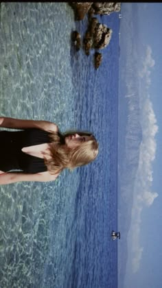 a woman in a black swimsuit standing next to the ocean