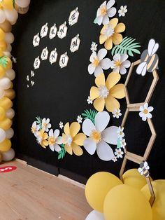 a black wall decorated with yellow and white balloons, paper flowers and honeycombs