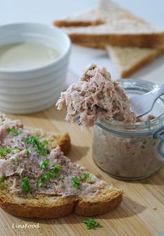 a piece of bread with meat spread on it next to a bowl of dip and some crackers