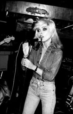 a black and white photo of a woman singing into a microphone while standing in front of two other people