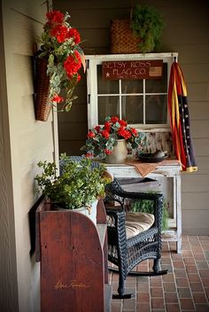 a porch with potted plants and flowers on the side of it, next to an old window