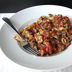 a white plate topped with pasta and meat on top of a table next to a fork