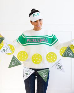 a woman in a white sweater is holding up some green and yellow pennants with the word pickleball on it