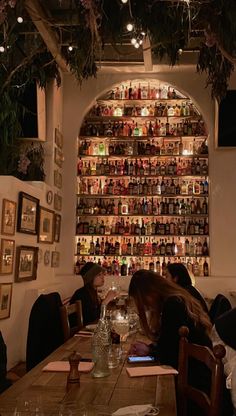 two women sitting at a table in front of a wall full of bottles