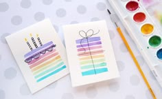 two cards with birthday candles on them next to paintbrushes and watercolors