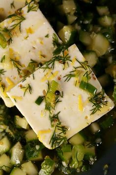 two square pieces of food sitting on top of a bowl filled with cucumbers