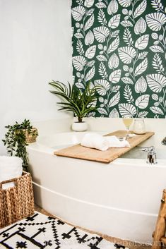 a bathtub with plants and towels on it in front of a patterned wallpaper