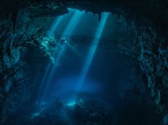 an underwater cave with sunlight streaming through the water and light beams coming from its ceiling